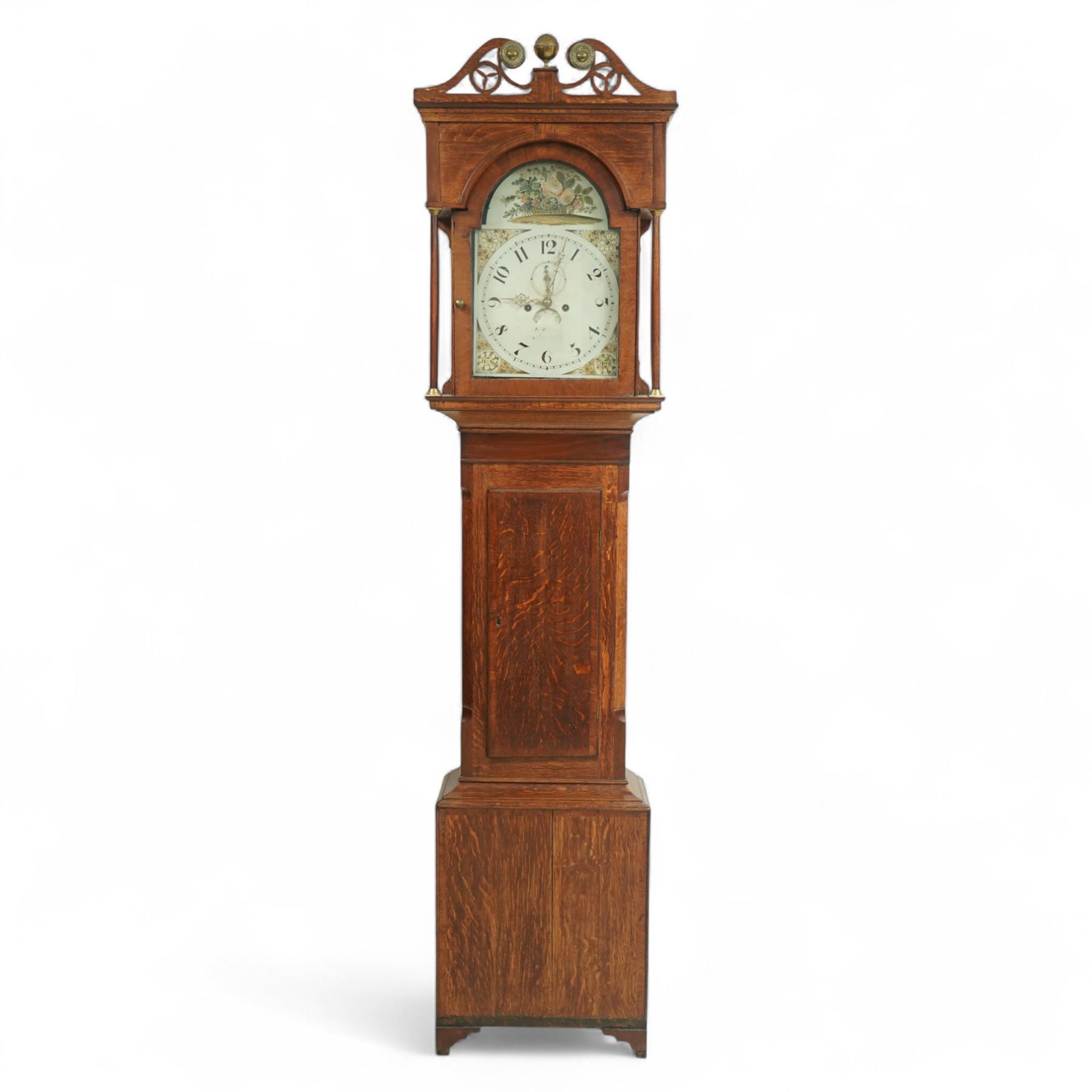 19th century-Oak and Mahogany 8-day longcase clock c 1820 (maker indistinct) with an open carved swan necked pediment and central finial, hood door flanked by turned pilasters, trunk with canted corners and a plain rectangular door, plinth with crossbanding and raised on bracket feet, painted dial with tumbling Arabic's, floral spandrels and conforming decoration to the arch, with a seconds hand, date aperture and brass stamped hands, dial pinned to a rack striking movement striking the hours on a bell. With weights & pendulum.