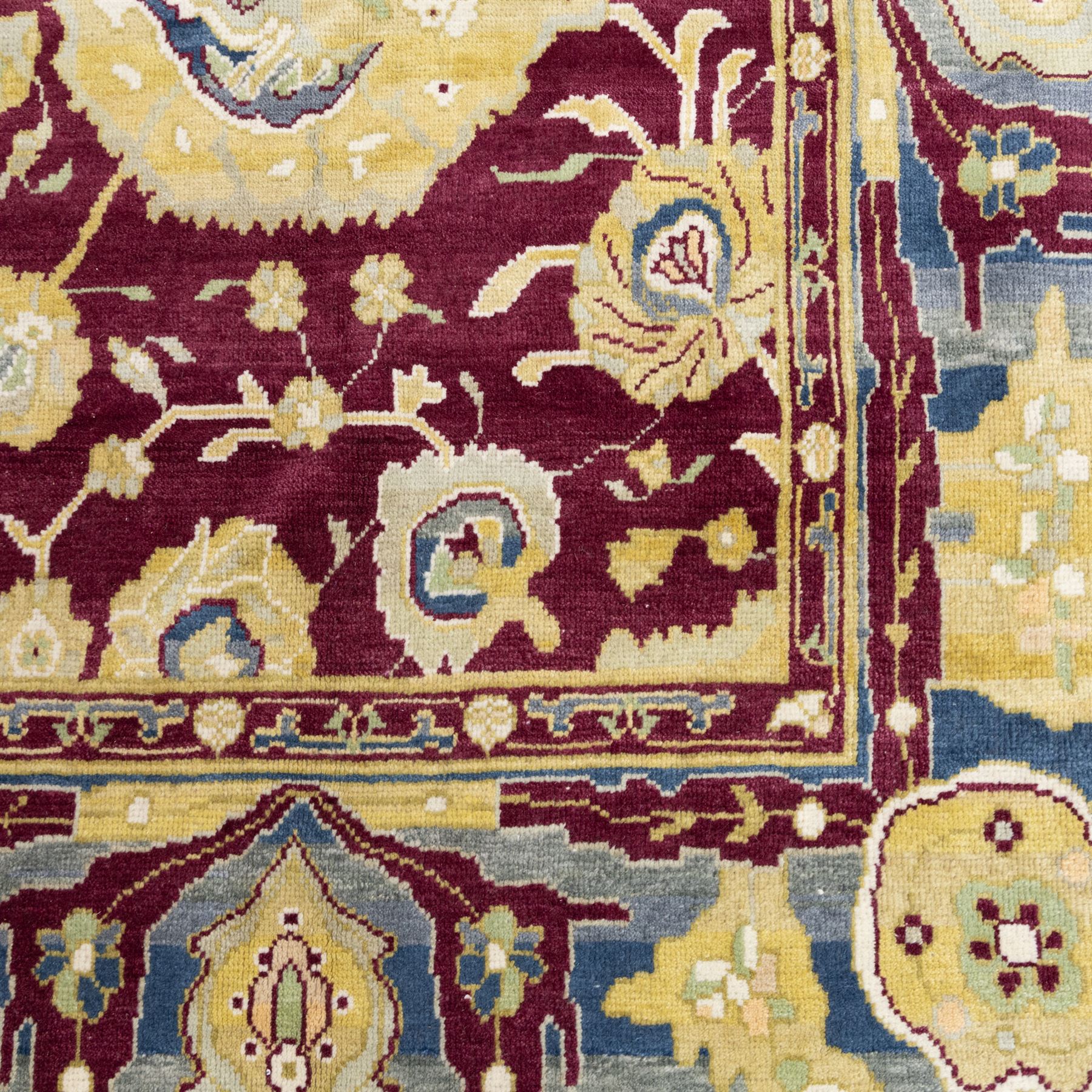Agra design wool carpet, burgundy field decorated with large scrolling floral vines, palmettes and flowerheads, enclosed by blue main border with oversized stylised palmettes and narrow guard stripes