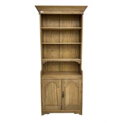 Light oak open bookcase cupboard, projecting cornice over three shelves, fitted with double cupboard enclosed by arched panelled doors 