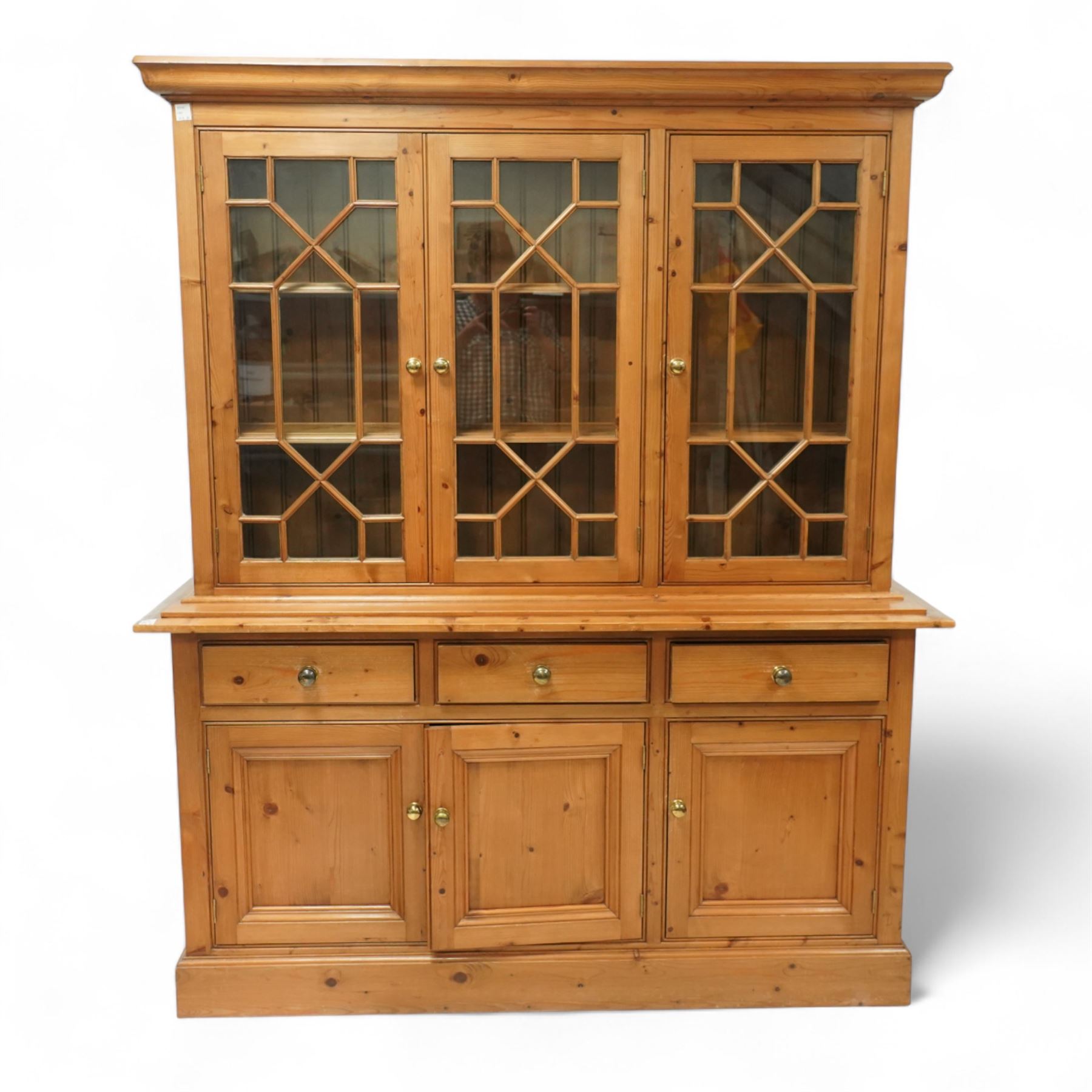 Mid 20th century pine glazed dresser on cupboard base, upper section of rectangular form with three astragal glazed hinged doors enclosing two adjustable wooden shelves and projecting frieze over three short drawers and three hinged panelled cupboard doors with brass handles, the front and sides, raised on a plinth base 