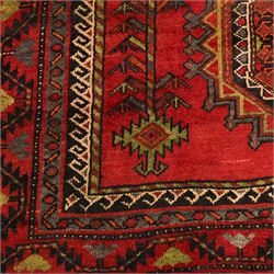 North East Persian Kurdish hand-knotted carpet, madder red field with three vertical and central stepped octagonal medallions enclosing angular geometric motifs with scattered tribal devices, framed by multiple narrow borders with latch-hook patterns, enclosing a bold main border of repeating geometric motifs, palette with indigo, dark brown and soft green tones, 