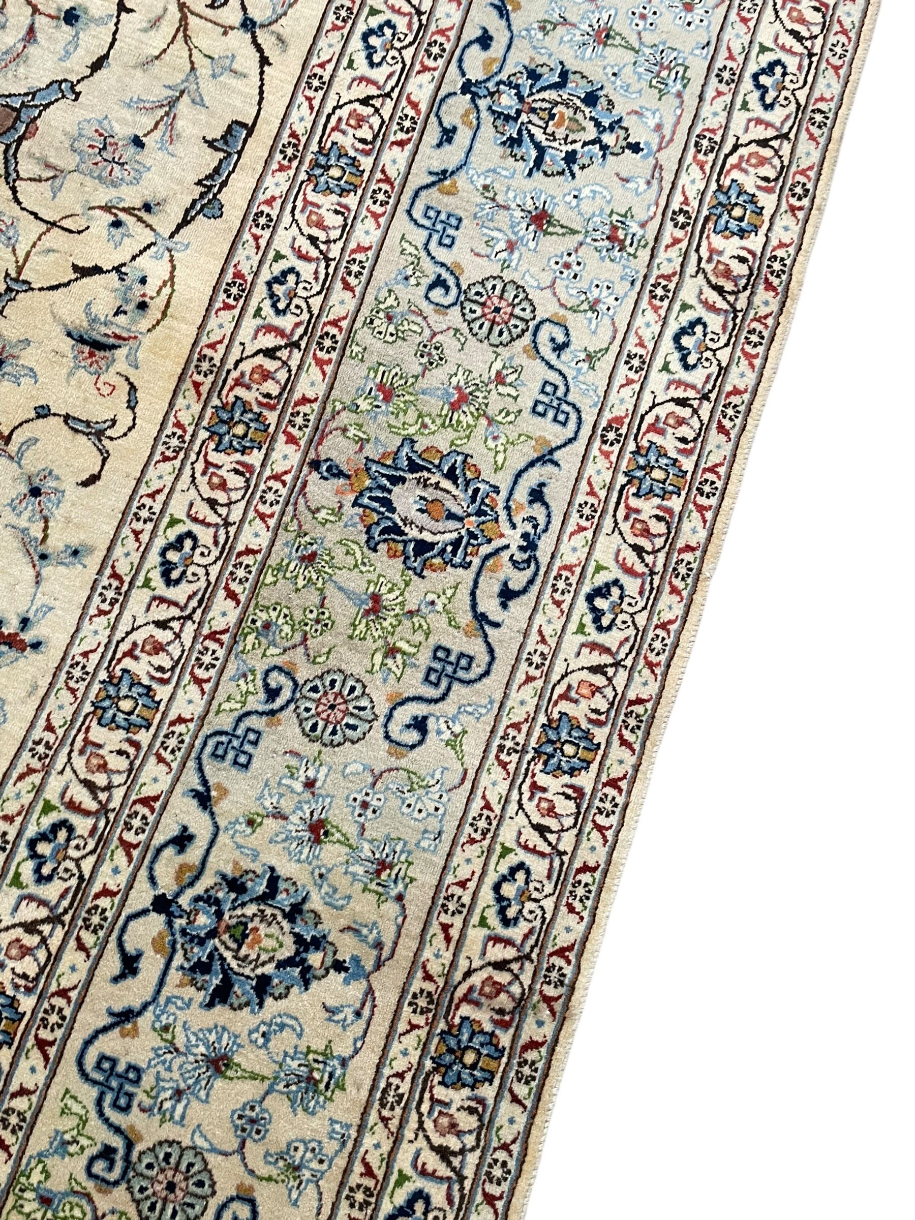 Persian Kashan ivory ground carpet, the field decorated with swirling foliate patterns and stylised plant motifs, scrolling border decorated with palmettes, within floral pattern guard stripes 