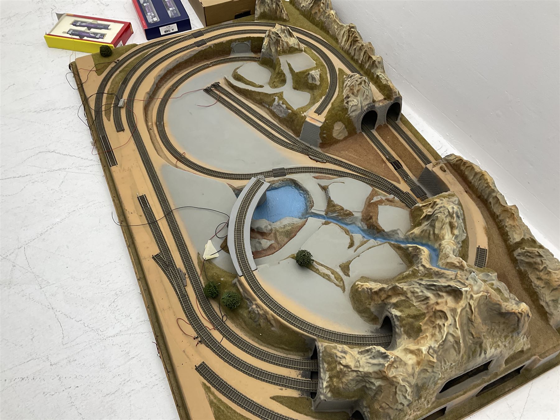 '00' gauge - table-top moulded plastic model railway layout with various rocky outcrops, tunnels, waterfall to lake, loops of Fleischmann track supplemented by Hornby track, bridges, kit built buildings and other accessories; together with Bachmann Class 150 2-car DMU Set and Hornby Northern Rail Class 142 2-car Set; both boxed; and small quantity of other rolling stock, three controllers etc  200 x 120cm