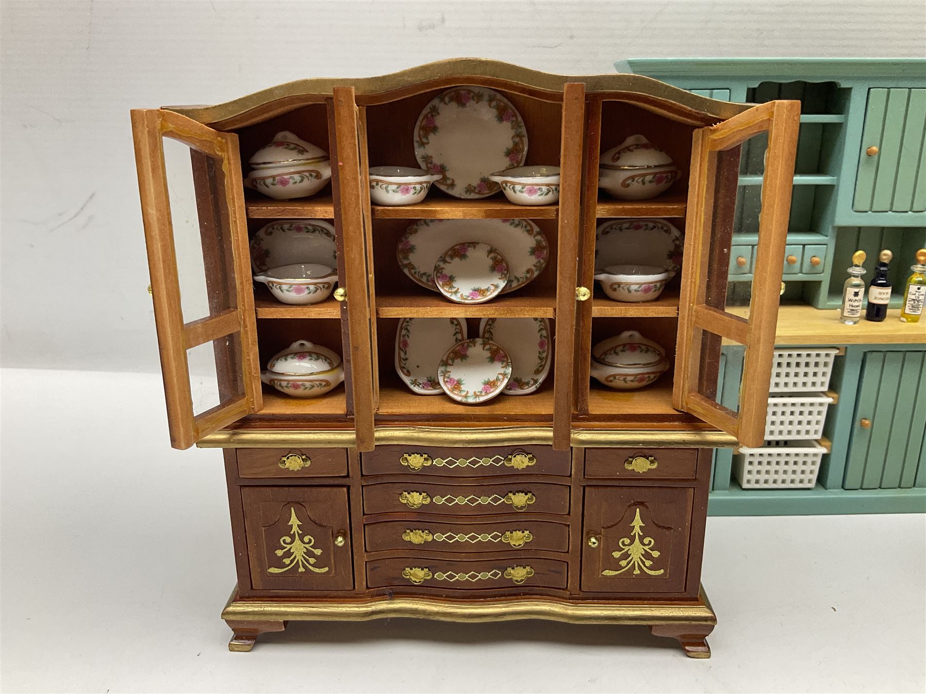 Collection of miniature dolls house furniture, to include display cabinet with pink and white floral dinner service, two serving trolleys with cakes and sweets and two blue painted kitchen dressers, together with miniature dolls house cardboard food packaging and animal figures including dogs and cats, etc