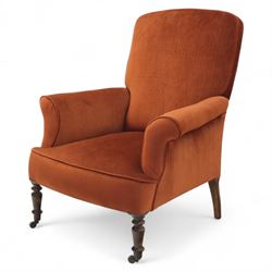 Late 19th century mahogany framed armchair, of generous proportion, upholstered in rust coloured velvet, with shaped back and scroll arms, raised on turned front legs with brass castors