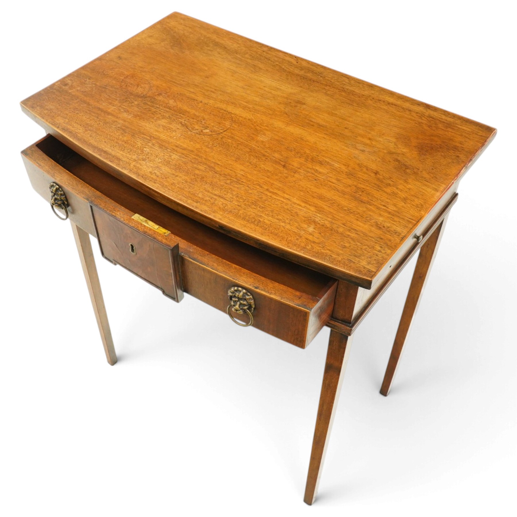 George III mahogany bowfront side table, fitted with single frieze drawer with brass lion-mask handles and twin candle-rests to each side, lower reeded edge on square tapering supports