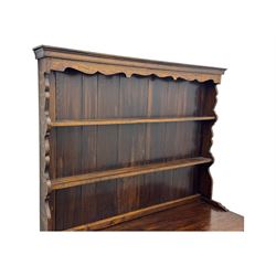 Late 19th century oak dresser, the upper section with two shelves beneath a shaped cornice, the lower section with a central bank of three drawers flanked by cupboard doors, all decorated with geometric diamond motifs, the drawers fitted with brass handles, raised on a shaped plinth base