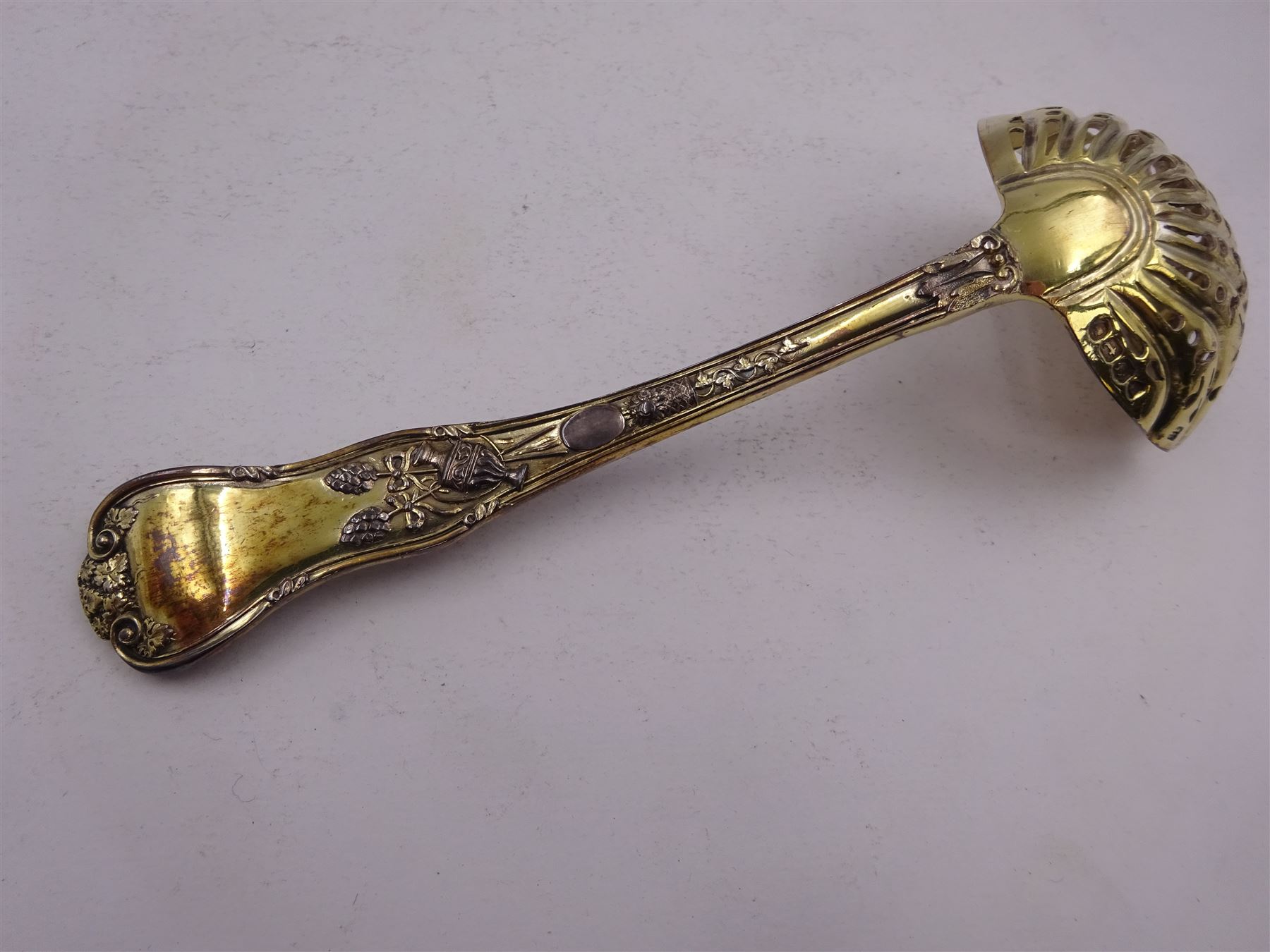 Victorian silver-gilt sugar sifting spoon, with gilded pierced shell shaped bowl, the handle decorated in relief with classical greek figures amongst fruiting vines, hallmarked Henry John Lias & James Wakely, London 1874,  L16cm, contained within tooled leather silk and velvet lined fitted case