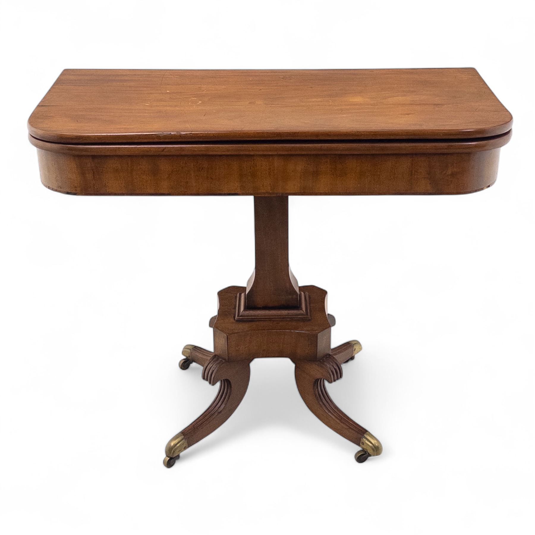 Regency mahogany fold-over table, hinged top with rounded corners opening to reveal a plain polished surface, supported on moulded pedestal base with reeded downswept legs, terminating in brass cups and castors (Extends to 90cm)