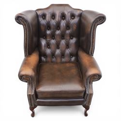 20th century Chesterfield style brown leather wingback armchairs, with button upholstered backs and wings, shaped scroll arms with studded borders, loose seat cushions, raised on cabriole supports with pad feet
