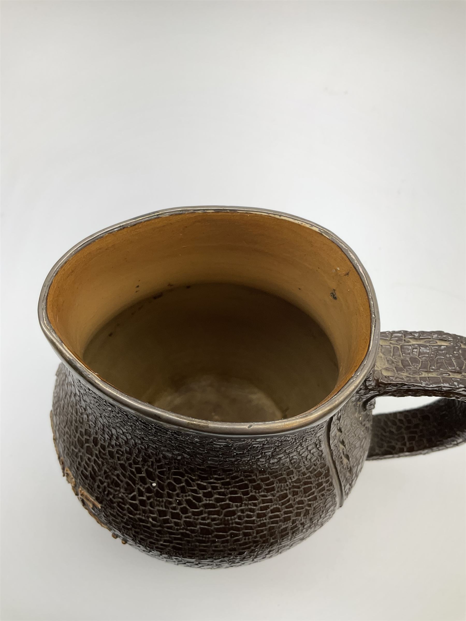 A Doulton Lambeth stoneware jug, with silver mounted collar, hallmarks rubbed, maker's mark probably Cornelius Desormeaux Saunders & James Francis Hollings (Frank) Shepherd, the leather effect body titled 'Drinke Faire Don't Sware', with impressed marks beneath including 'Manufactured for Sidney W Allen 39 White Rock Hastings', H18.5cm. 