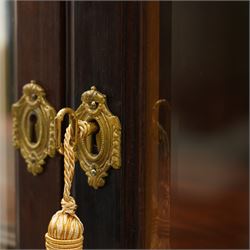 Large and impressive 19th century heavily carved mahogany display cabinet, the ornate pediment carved with a central scalloped and foliate rocaille motif with extending acanthus leaves and egg-and-dart moulding flanked by acanthi finials, over a central cartouche with carved bow-and-arrow motif and trailing scrollwork, the bookcase enclosed by two glazed doors with bevelled glass sides, the base with a gadrooned upper edge over a central rocaille ornament with scrolling acanthus leaves, the panelled frieze with further foliate motifs, raised on large carved snarling lion mask supports with floral garlands and claw feet, united by a concave rectangular platform base with gadrooning egg-and-dart moulding