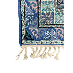 Morrocan single weft blue ground rug, the field segmented into a grid of ten rectangular panels, bordered by a series of guard bands with repeating floral and geometric patterns with interlocking vines and rosettes, the edges finished with a fringe of twisted tassles