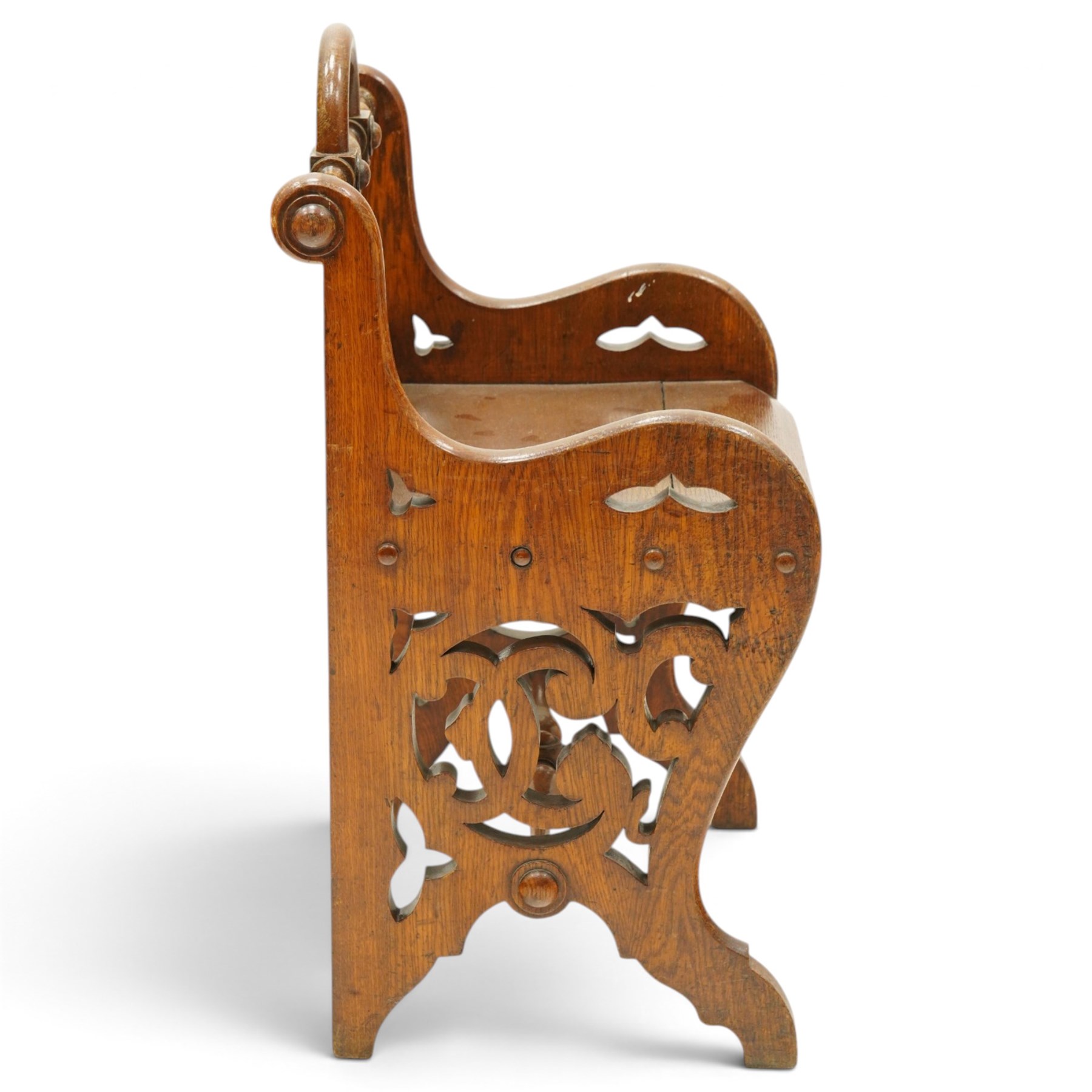 Late 19th century Gothic Revival carved oak hall chair or window seat, the swell-turned top rail centred by an arched carrying handle, over shaped open arms and solid plank seat, with pierced and carved scrolling foliate fretwork side panels and apron with applied central roundel, raised on shaped supports united by turned stretcher