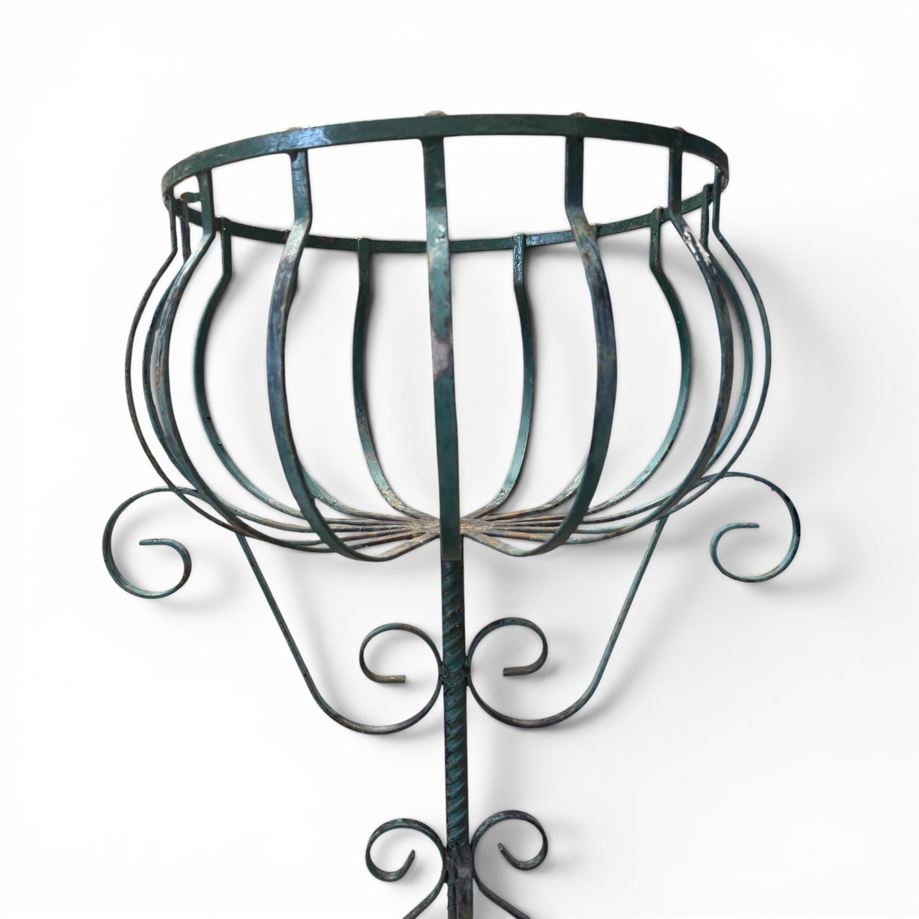Matched pair of antique metal plant stands, each with circular strapwork basket tops, the scrollwork supports raised on an X-form base, in green painted finish with rustic patina
