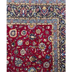 Northeastern Persian Meshed hand-knotted carpet, madder red field with an all-over design of scrolling vines, palmettes, and rosettes, within a dark blue border of palmettes and arabesques 