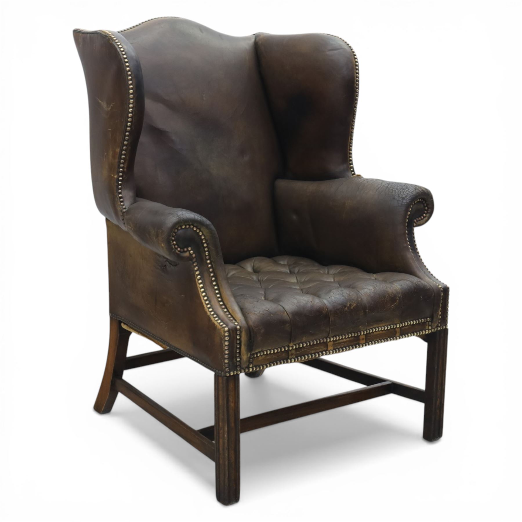 Georgian style leather wing armchair, shaped high back with outscrolled wings above padded arms and deep buttoned seat, close-nailed throughout, raised on square supports united by H-stretcher