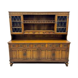 Large mid-20th-century oak dresser with two astragal glazed doors between gallery shelf and lower shelf, with three short drawers and lower section with four drawers and three double-panelled linen-fold hinged cupboard doors 