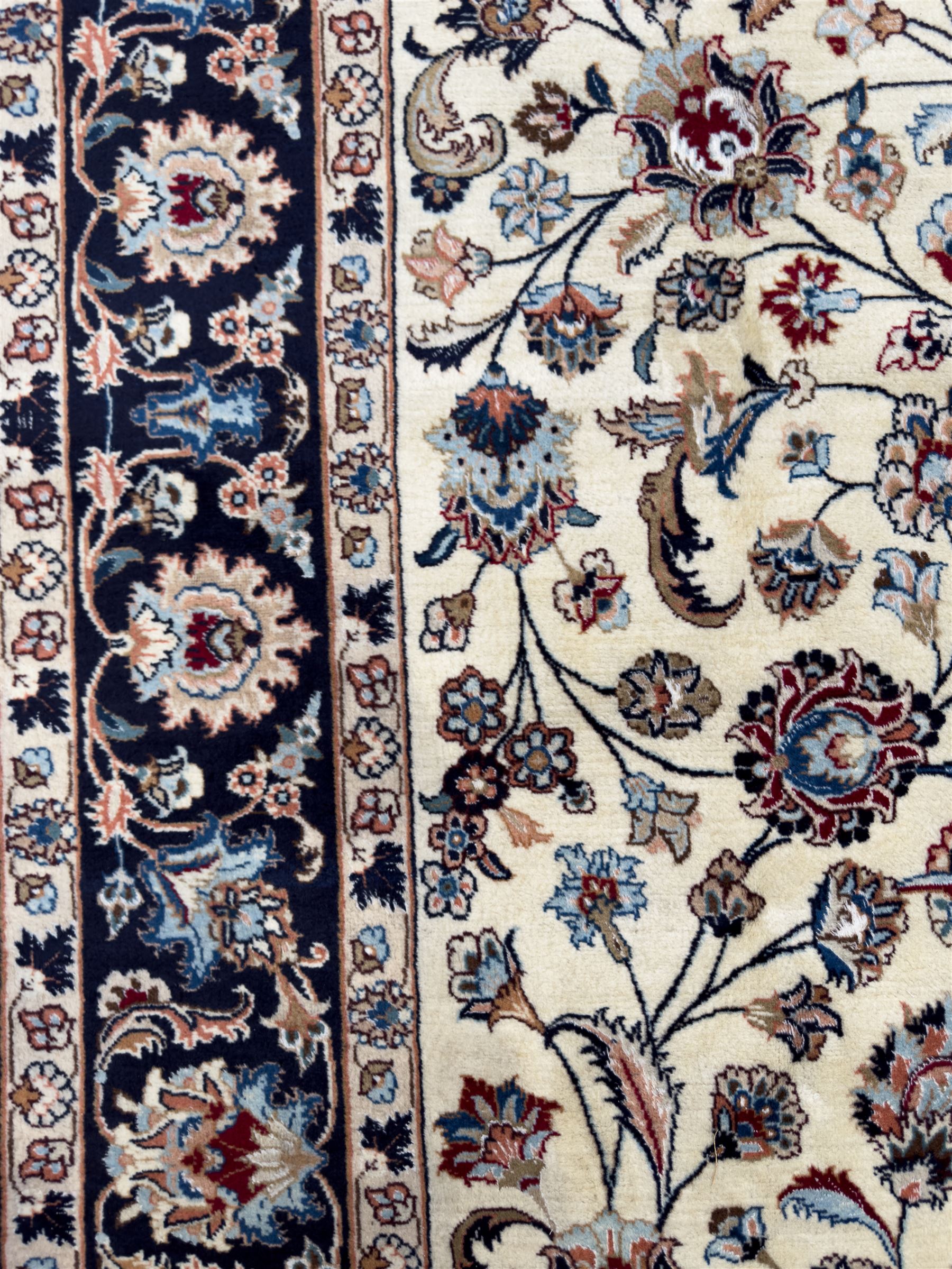 North East Persian Meshed hand-knotted rug, ivory field with scrolling vines, palmettes, and rosettes in shades of blue and brown, within a dark blue border of palmettes and flowerheads between multiple guard stripes, with cotton fringe ends  
