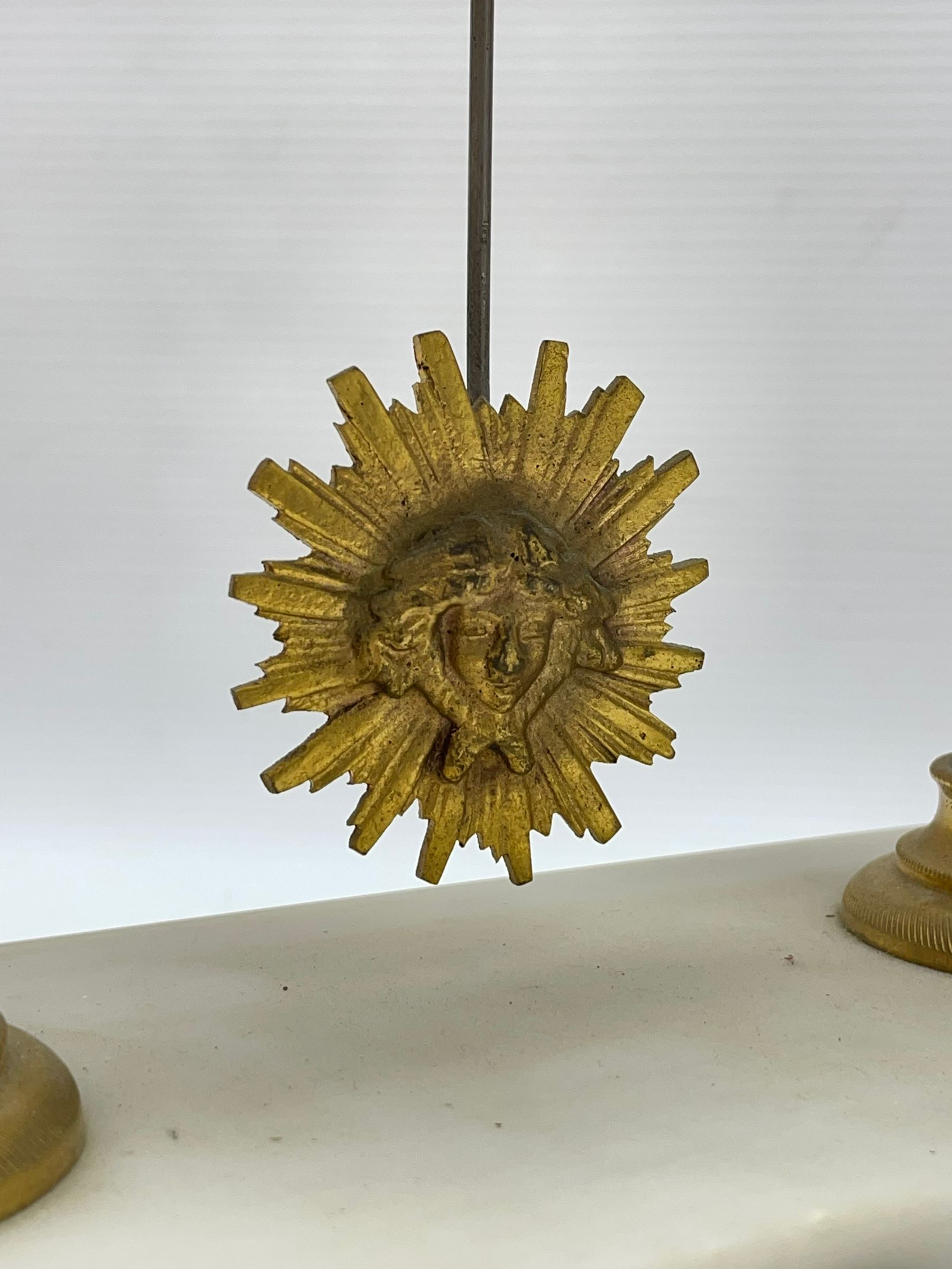 French - Late 19th century 8-day white marble and gilt metal portico clock garniture, the clock surmounted by an urn and raised on a pair of cylindrical pillars above a rectangular plinth base, white enamel dial with Arabic numerals and floral garlands, twin train countwheel striking movement, striking the hours and half hours on a bell, with a sunburst pendulum and gilt Louis XVI hands, garniture with matching twin light candelabra. With Key.   Candelabra H 30cm.