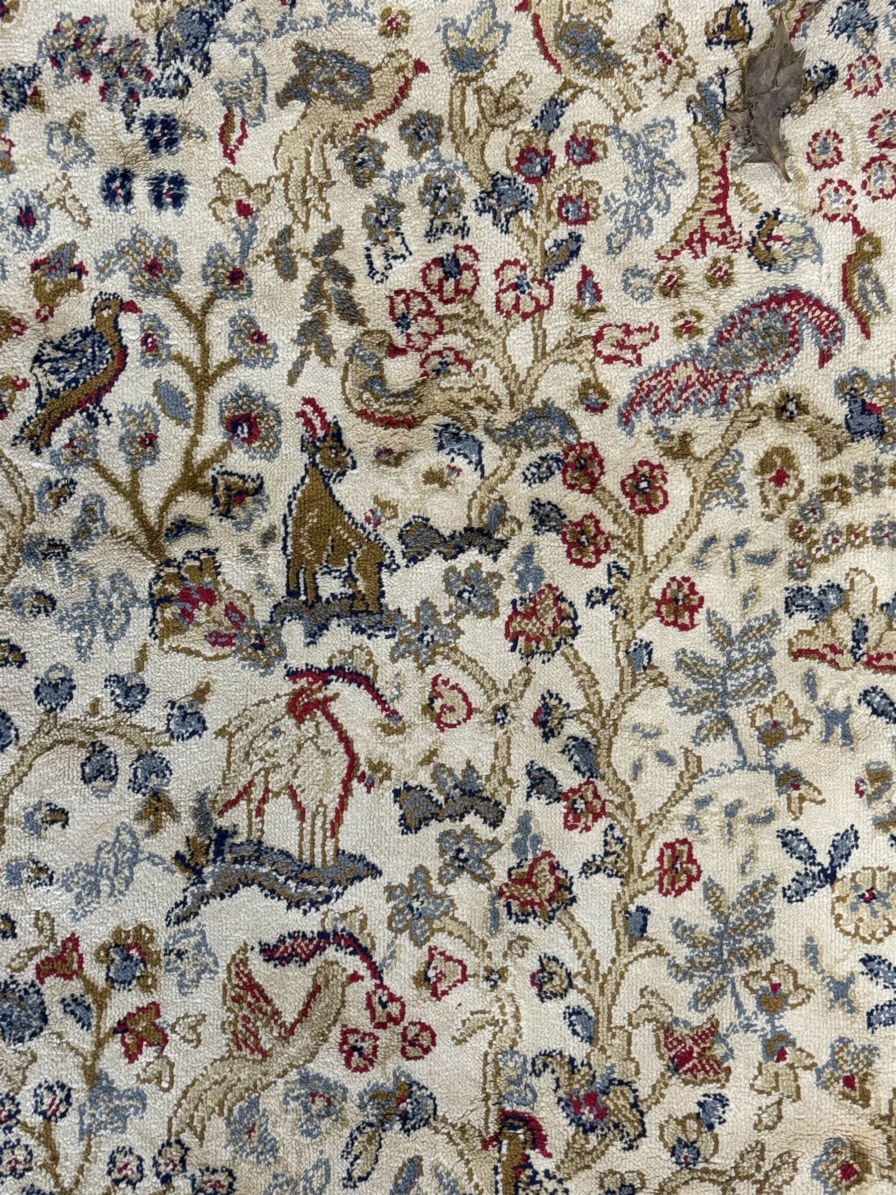 Persian Kerman ivory ground rug, the field adorned with naturalistic depictions of birds, animals and floral designs, framed by a multi-band border in blue and red tones