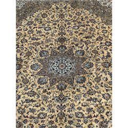 Central Persian Kashan pale khaki and ivory ground carpet, shaped central medallion enclosing small stylised motifs, the field decorated profusely with trailing foliate branches and plant motifs, guarded border with repeating floral design
