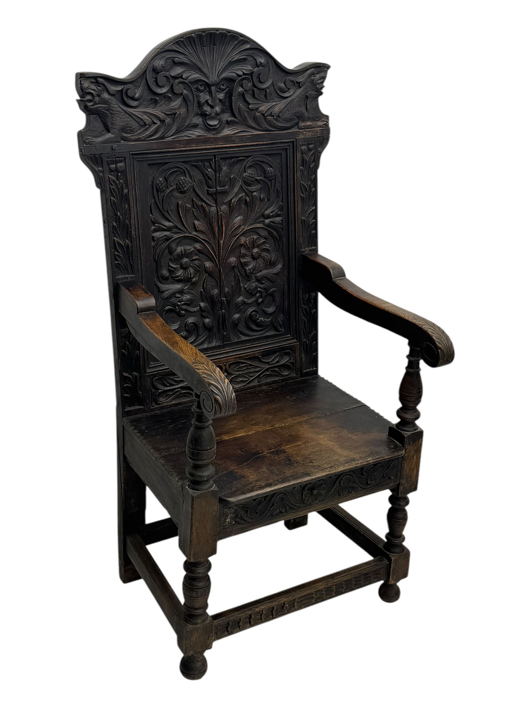 Late 19th century Jacobean revival carved oak armchair, the tall back with arched cresting featuring a stylised foliate mask, flanked by carved scrolls, relief carved panel depicting symmetrical foliage, downscrolled arms, on turned front supports united by stretchers