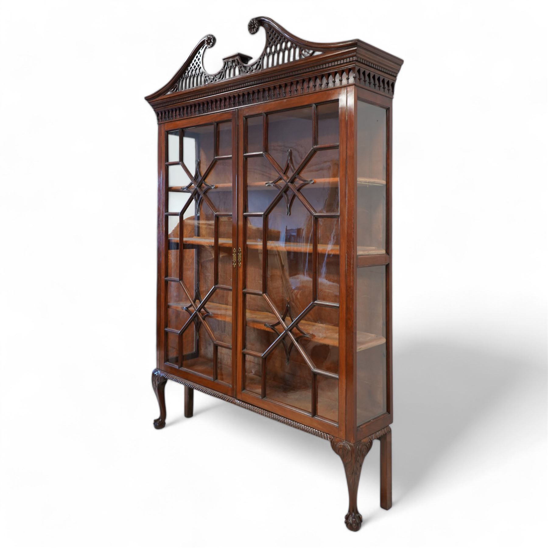 Large George III mahogany bookcase display cabinet, pierced swan neck pediment with floral head roundels over dentil and arcade frieze, enclosed by two geometric astragal glazed doors with lozenge motifs, the lined interior fitted with three shelves, gadrooned lower rail over acanthus carved cabriole supports with ball and claw feet 

