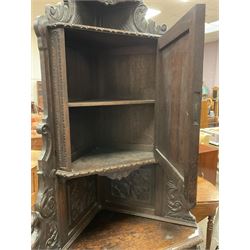 Victorian heavily carved oak corner cupboard, raised shaped back with shelf carved with scrolling foliage, the upper and lower cupboards enclosed by panelled doors with applied mouldings and masks, canted corners with carved leaf and berry decoration 