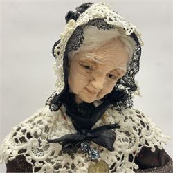 Anna Meszaros Hungary - hand made needlework figurine 'Old Lady' seated on a stool wearing a lace trimmed black/white/red floral full length dress and hat, working on a piece of lace H30cm  Auctioneer's Note: Anna Meszaros came to England from her native Hungary in 1959 to marry an English businessman she met while demonstrating her art at the 1958 Brussels Exhibition. Shortly before she left for England she was awarded the title of Folk Artist Master by the Hungarian Government. Anna was a gifted painter of mainly portraits and sculptress before starting to make her figurines which are completely hand made and unique, each with a character and expression of its own. The hands, feet and face are sculptured by layering the material and pulling the features into place with needle and thread. She died in Hull in 1998.
