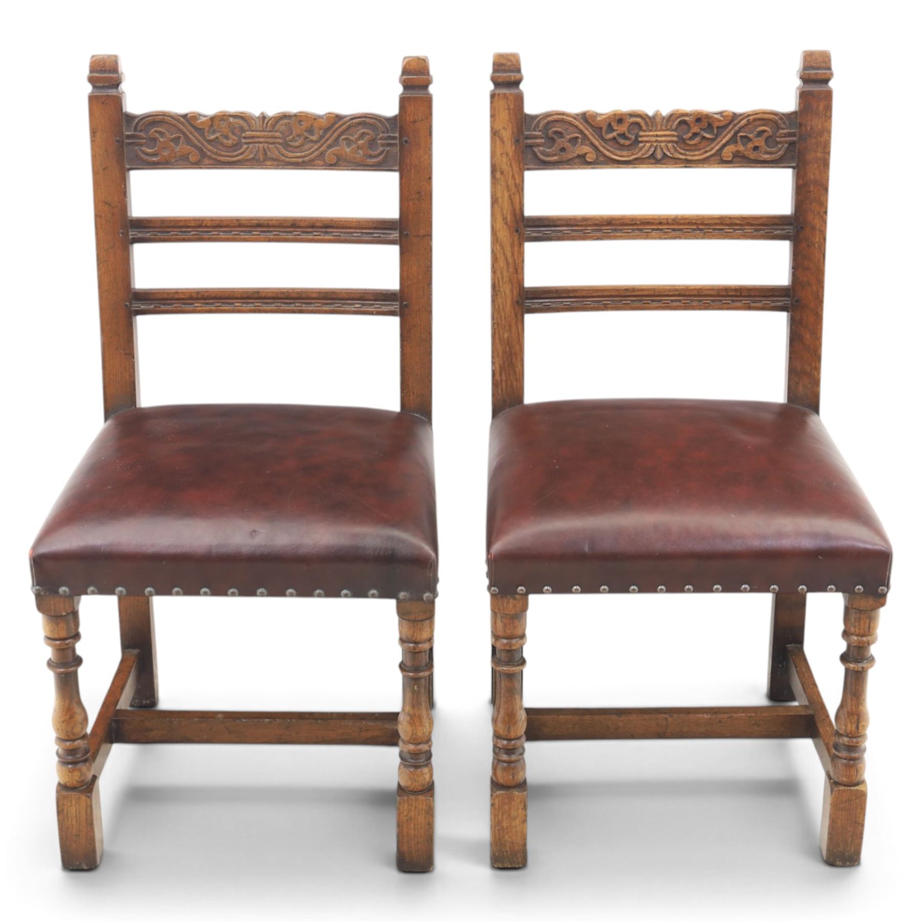 Craftsman made set of four solid oak dining chairs with leather seats, with carved cresting rail, on red leather seats with studded trim, raised on block and turn supports united by H-stretcher