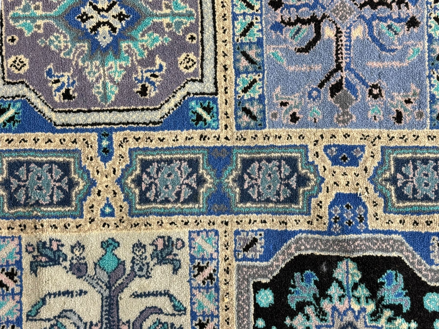 Morrocan single weft blue ground rug, the field segmented into a grid of ten rectangular panels, bordered by a series of guard bands with repeating floral and geometric patterns with interlocking vines and rosettes, the edges finished with a fringe of twisted tassles