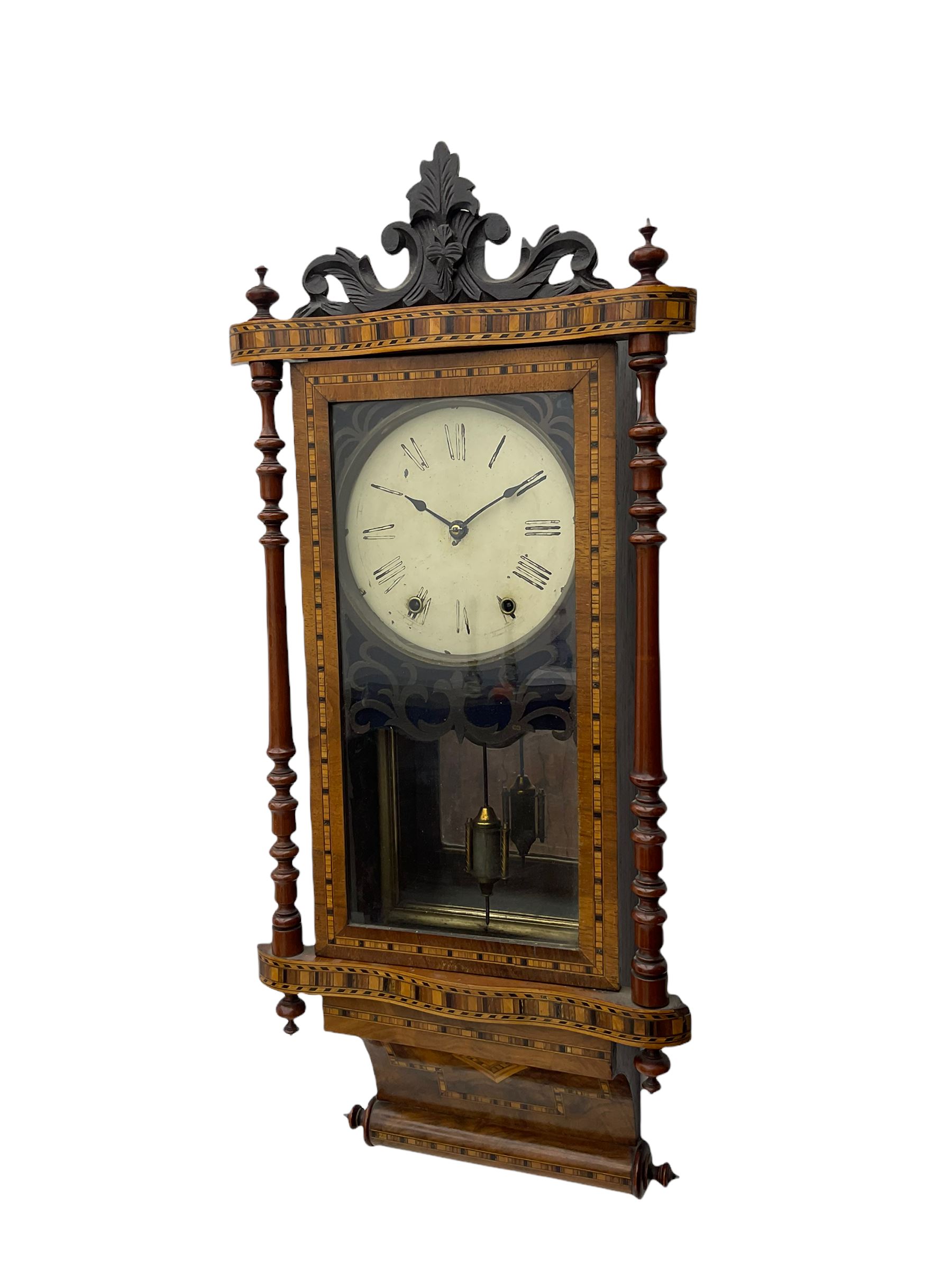 A late 19th century spring driven American Eight-day wall clock, striking the hours on a bell, in a parquetry case with contrasting oak, maple, walnut, and other hardwoods, with a flat top, carved cresting and finials rectangular glazed door flanked by finely turned pilasters, with a painted dial with roman numerals and minute track, steel spade hands and faux mercury pendulum reflected in a rear case mirror.   


