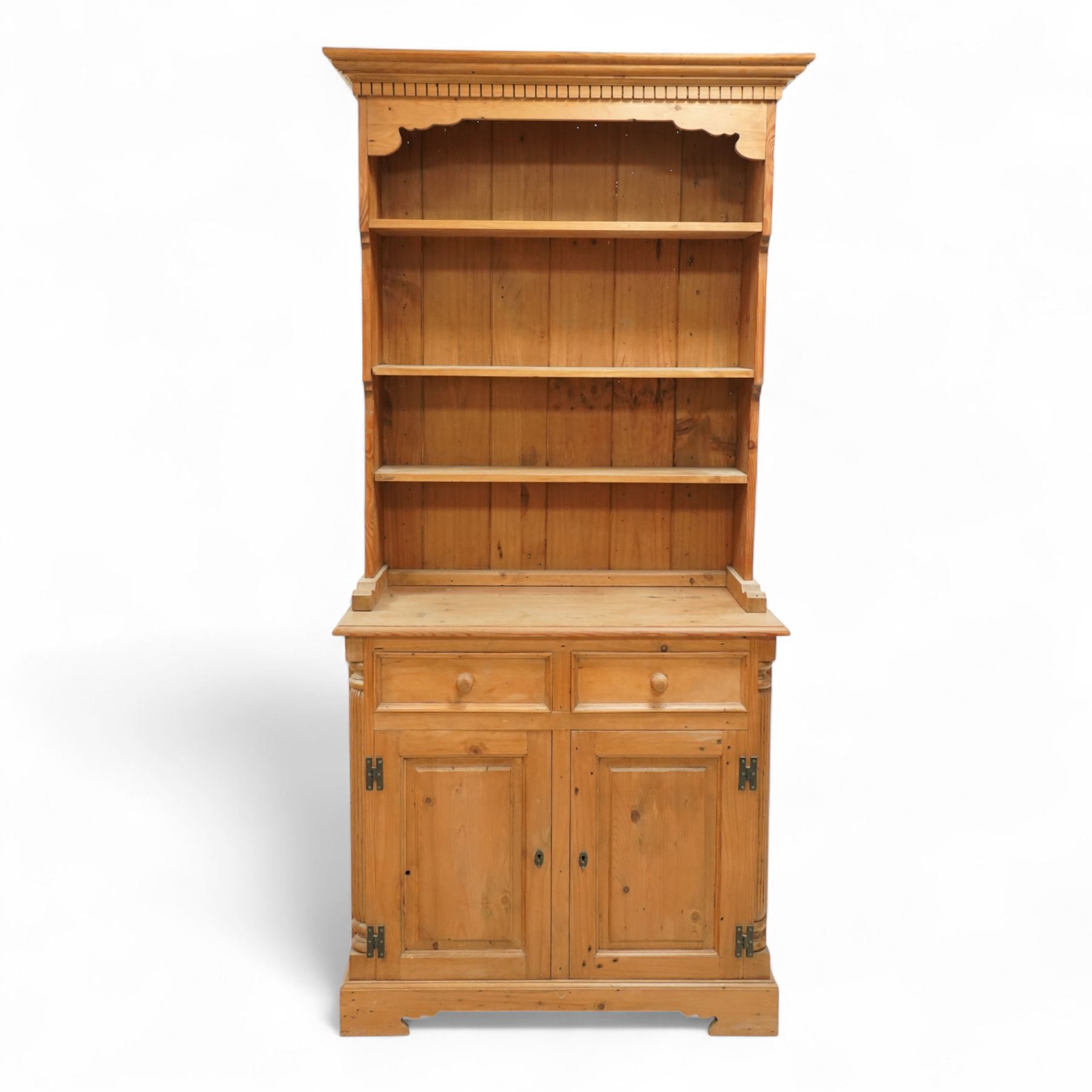 20th century stripped pine dresser, the open rack with dentil frieze and fixed shelves over a cupboard base with two drawers and fielded panel doors, flanked by stop-fluted uprights, on a moulded plinth