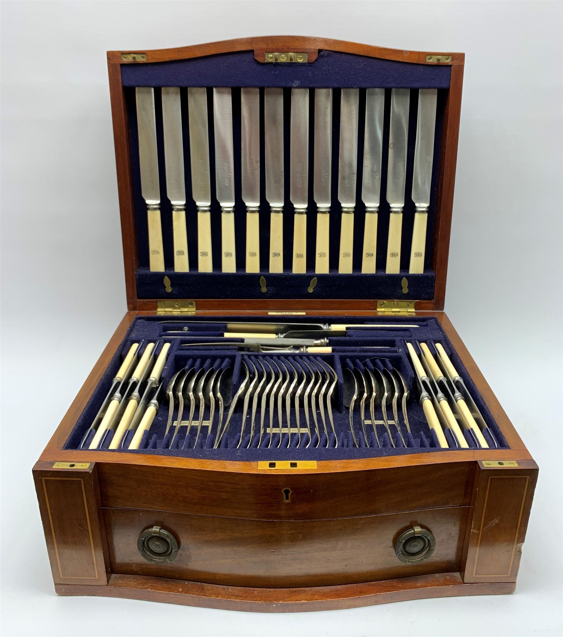 Late 19th/early 20th century composite canteen of silver flatware, contained within an early 20th century mahogany serpentine fronted case with twin drop carry handles, and hinged cover with boxwood stringing and central inlaid shell motif, above a single drawer with twin ring handles and Wellington style locking system, the cover and drawer opening to reveal plaque for Spink & Sons Ltd London, and fitted interior containing ivory handled knives, ivory handled carving set, and silver Hanoverian and Old English pattern cutlery, each with engraved monogram to terminal, hallmarked London, makers Spink & Son (John Marshall Spink), Goldsmiths & Silversmiths Co, and Chawner & Co (George William Adams), various dates ranging 1880-1923, gross weighable silver 92.59 ozt (2880 grams)