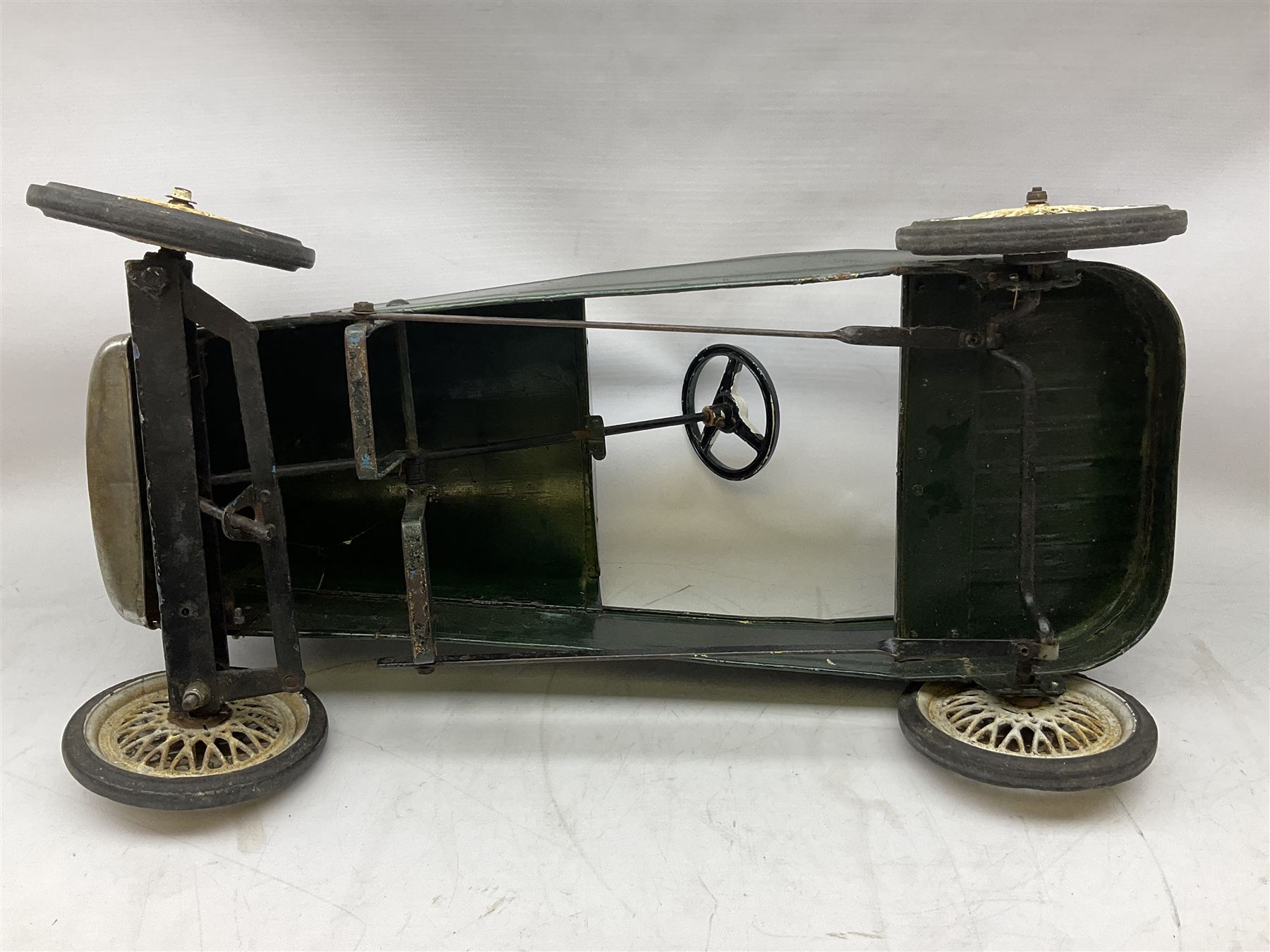 Mid 20th century pressed steel pedal car, the body painted in dark green fitted with pretend radiator to the bonnet, with spoked wheels and rubber tyres, the interior with pedals and steering wheel, L70cm