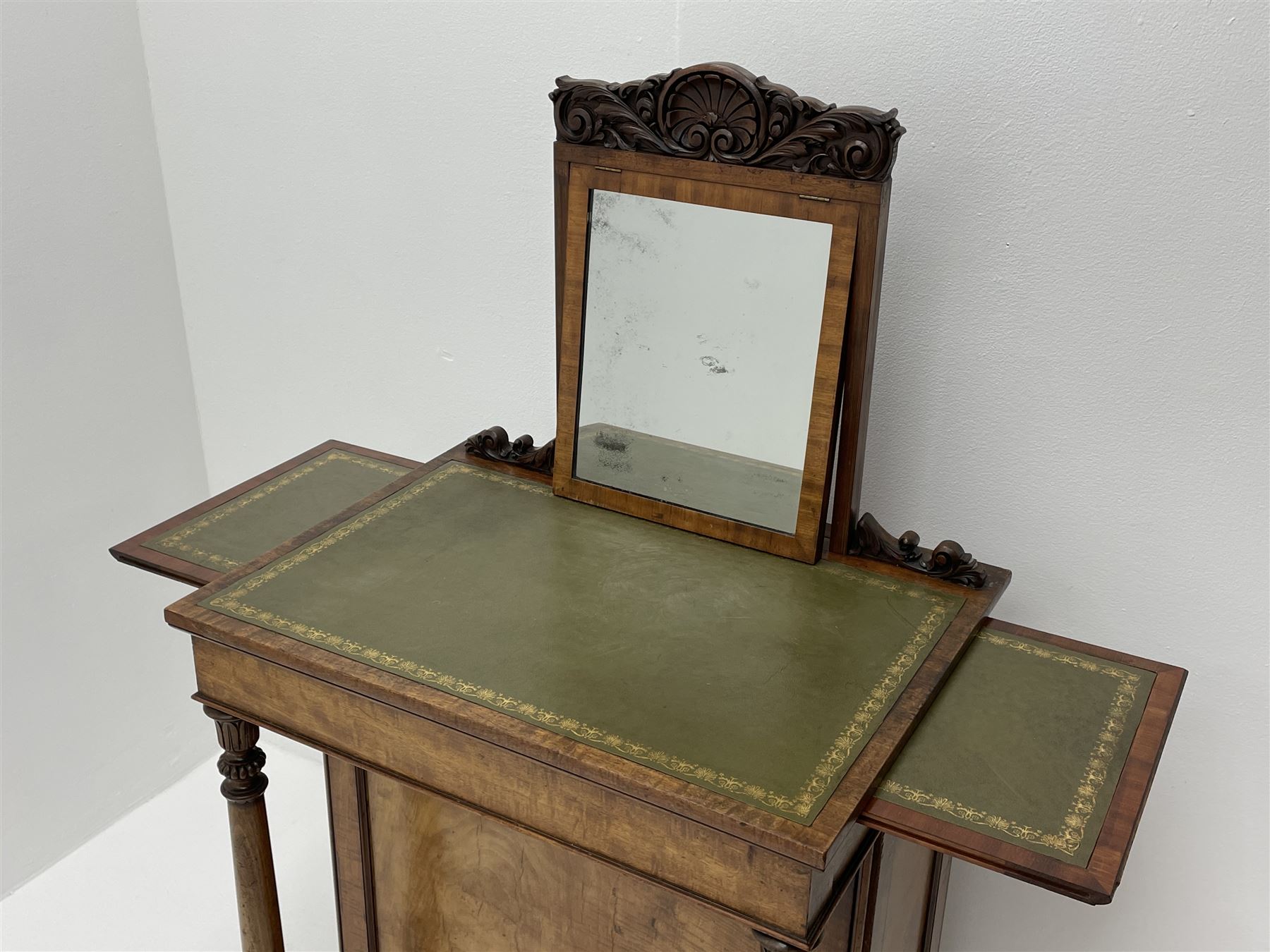 Early Victorian figured mahogany dressing cabinet, the raised shell and scroll carved back lifts to reveal rectangular easel mirror with mahogany band, flat rectangular top with tooled leather inset, slide at each side with matching leather inset, full width drawer above cupboard enclosing a series of five drawers, turned front supports, panelled front, sides and back