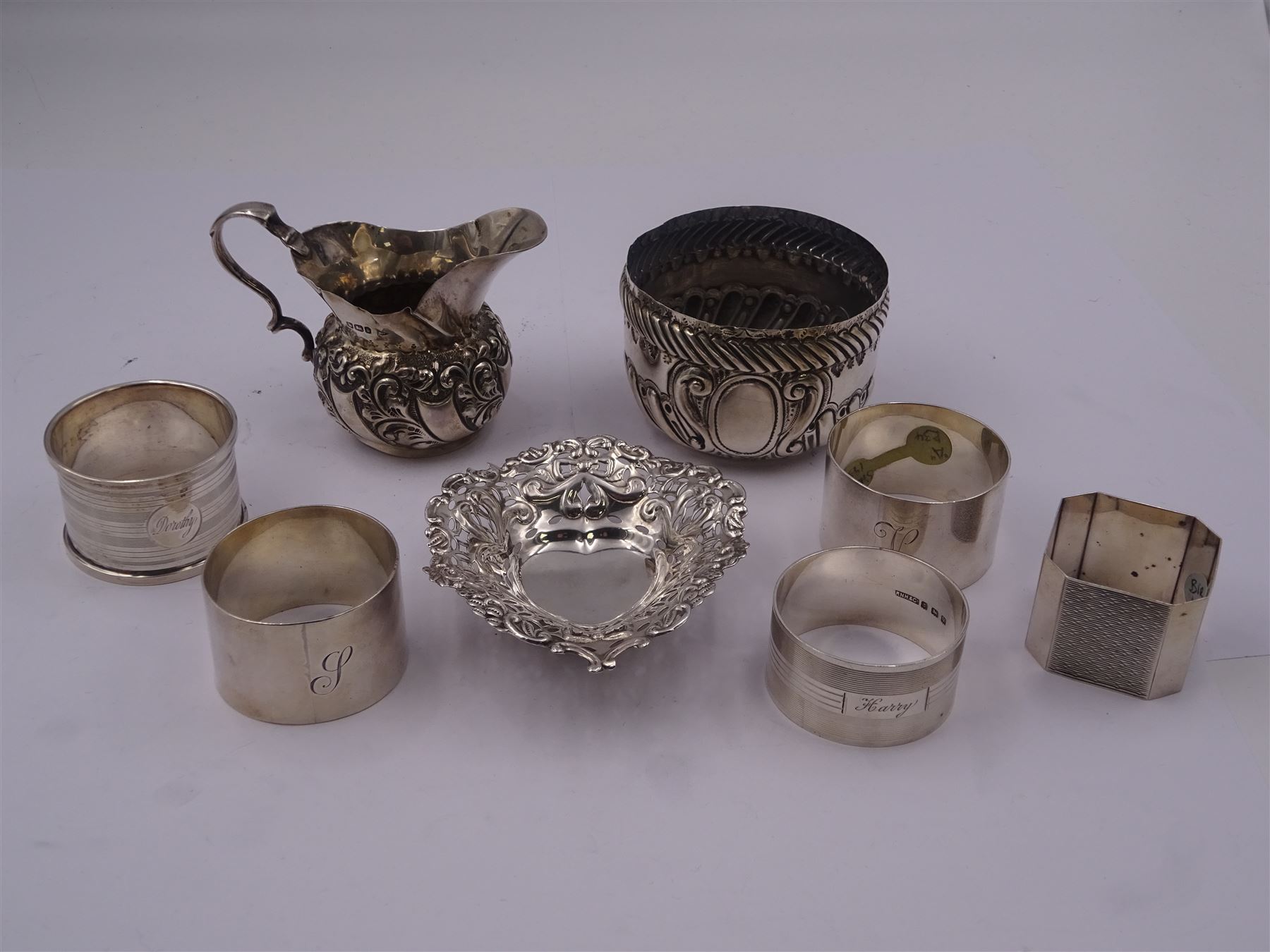 Group of five mid 20th century silver napkin rings, comprising a pair of plain circular form engraved with initial, hallmarked Viner's Ltd, Sheffield 1932, a circular example with engine turned bands, hallmarked R N Hollings & Co, Birmingham 1945, and two further 1930's examples, hallmarked Birmingham 1930 and 1934, various makers, together with a small early 20th century silver cream jug, of bellied form with foliate embossed decoration and scroll handle, hallmarked Walker & Hall, Sheffield 1910, including handle H6.5cm, etc.,  approximate total weight 8.98 ozt (279.3 grams)