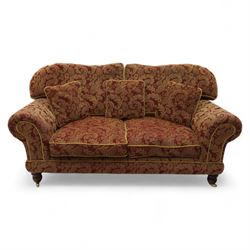 Duresta - two seat settee, upholstered in red and gold damask fabric with piped edges, scroll arms and loose feather-filled cushions, raised on turned wooden feet with brass castors