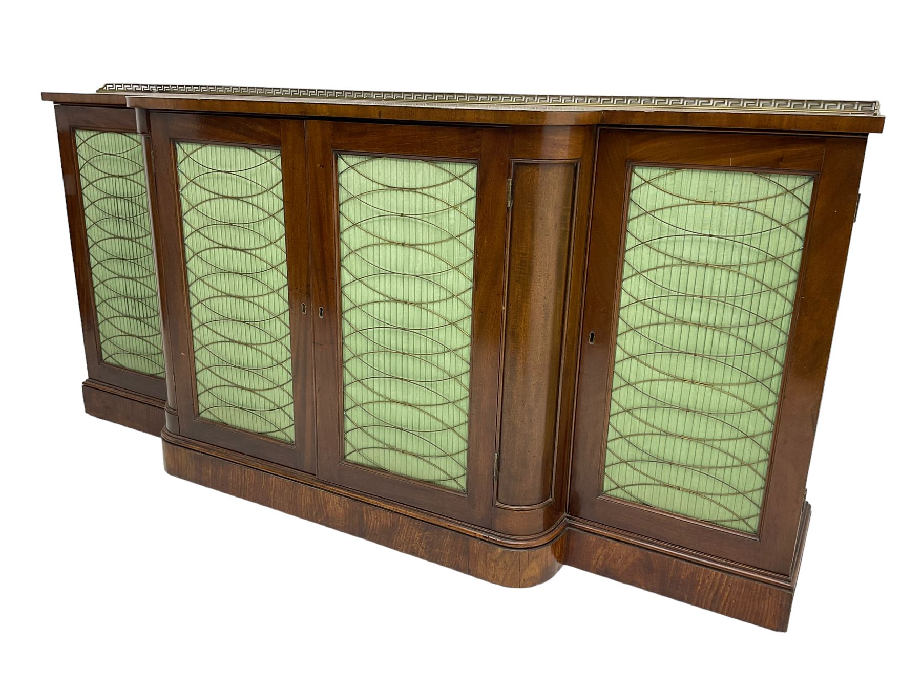 19th century mahogany break-front sideboard, raised brass gallery back with Greek key design, fitted with four cupboard doors, their pleated green fabric overlain with gilt metal grilles, lower moulded edge over plinth base