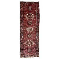 Persian Karajeh crimson ground runner rug, the field set with seven geometric lozenge medallions, the field decorated all over with stylised plant motifs, the banded border with repeating geometric shapes and patterns