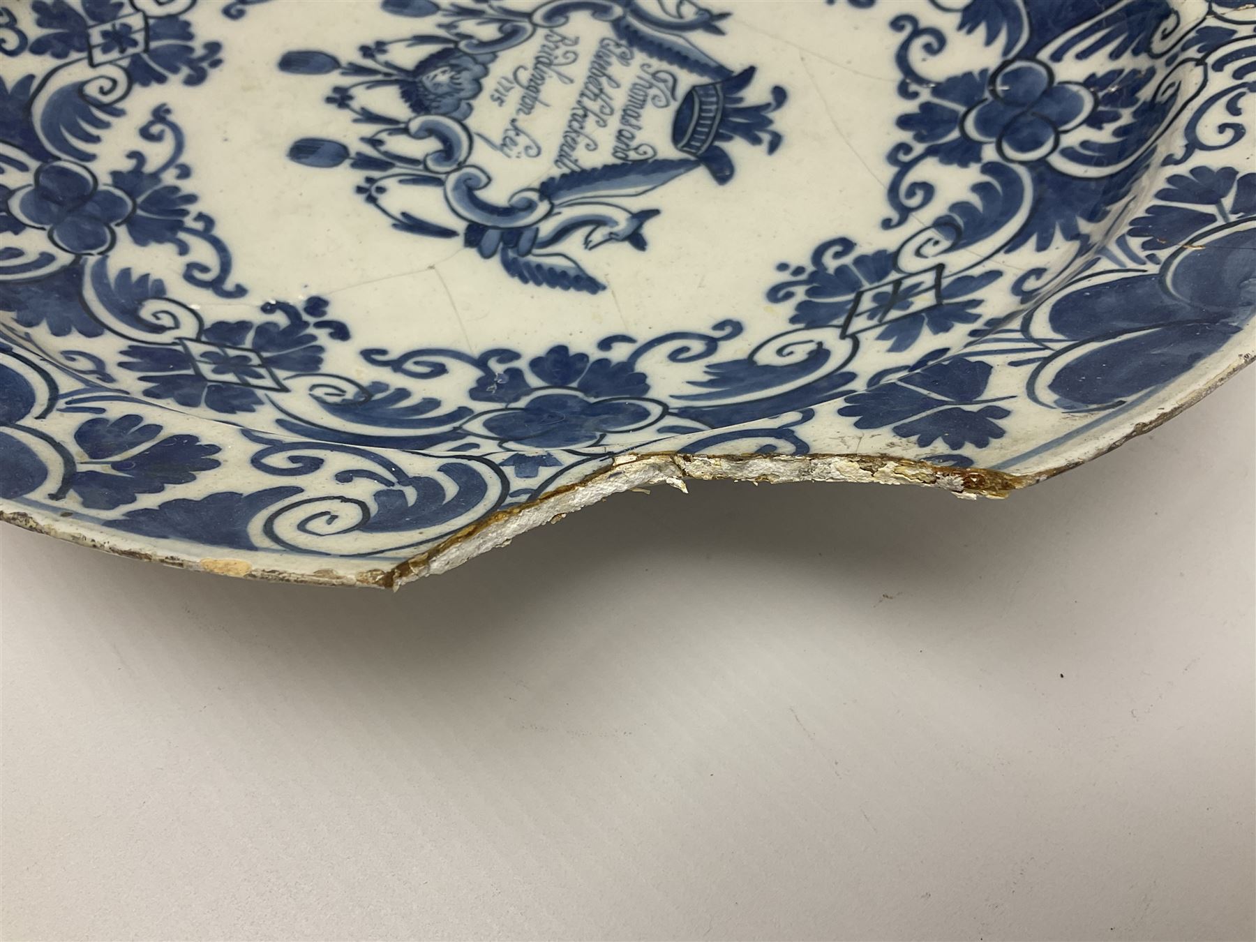 Early 18th century Delft marriage plate, of circular form with dished centre, the centre inscribed and dated 'Thomas and Elizabeth Kockerill Bridlington Key 1715' within a crowned C scroll cartouche, flanked by demi-griffins, above a putto head and tassels, within a wide foliate border, D34cm
