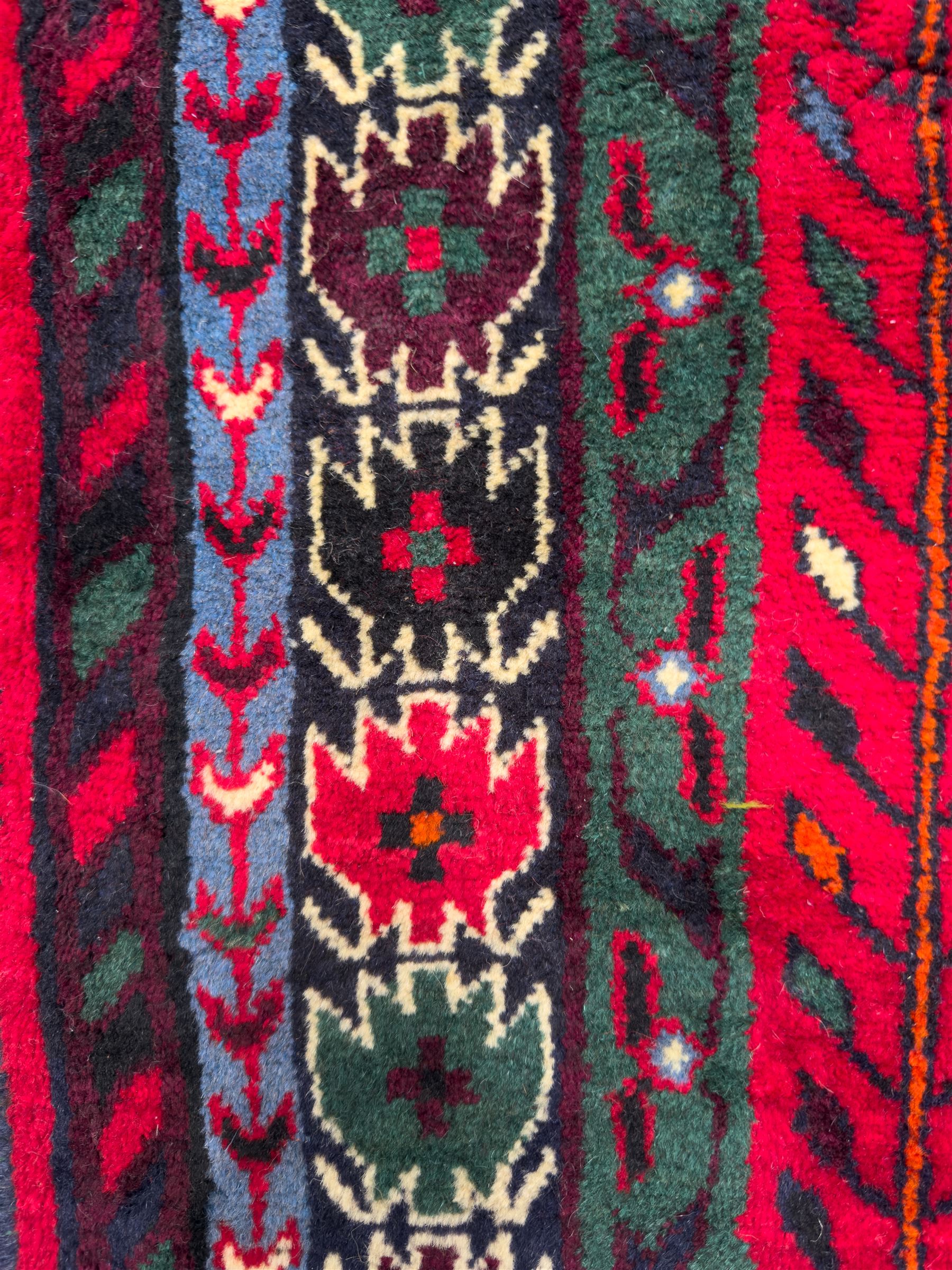 Northwestern Persian Cirjan hand-knotted carpet, madder red field with three linked stepped lozenge medallions in blue, ivory and green, flanked by angular motifs within a dark green border of serrated leaves and rosettes 