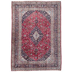 Central Persian Kashan crimson ground carpet, central  floral pole medallion with matching spandrels within a field of scrolling palmette motifs and foliage, the heavily banded indigo border with repeating plant motifs interlaced with scrolled branches