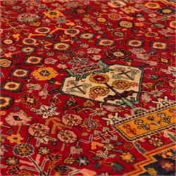 North Persian crimson ground rug, the field densely decorated with stylised flowering plants, urns and polychrome rosettes, within a stepped ochre outline, dark ground floral spandrels and geometric side panels
