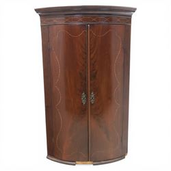 George III mahogany bow-front corner cupboard, projecting moulded cornice over satinwood inlaid frieze with geometric crossbanding, enclosed by twin shaped panel doors with line inlay and ornate brass escutcheon plates, painted interior fitted with shaped shelves, on moulded plinth base