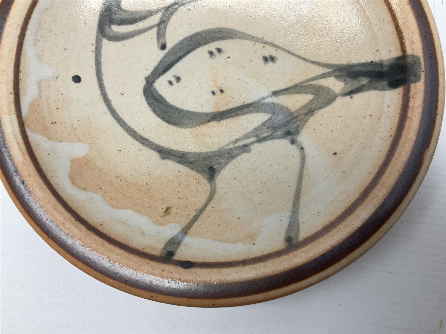 Studio pottery bowl, probably by Svend Bayer of Wenford Bridge, the stoneware body of shallow circular footed form with brushwork decoration of a stylised bird figure in grey upon peach ground within bands of iron red, unmarked, D18.5cm