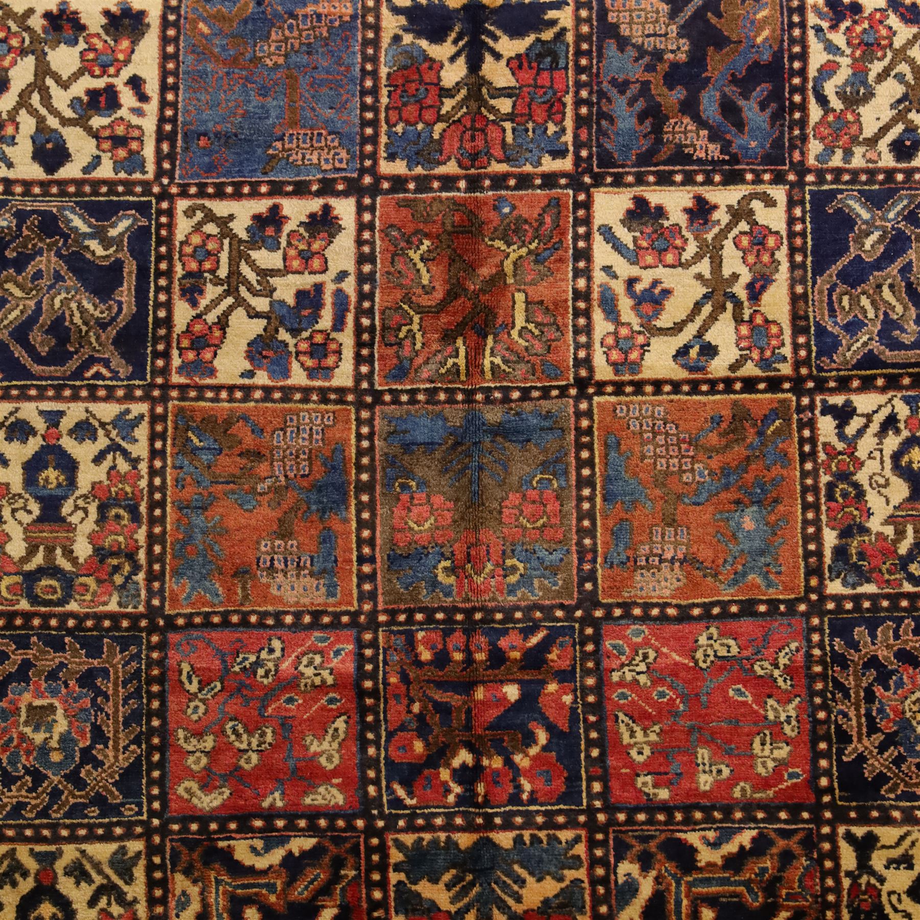 Central Persian Bakhtiari Kheshti design hand-knotted rug, field composed of a grid of square panels, each containing stylized floral devices, animal and foliate motifs woven in a rich palette of madder red, indigo blue, ivory ochre and brown, framed by a multiple striped border with a meandering vine and flowerhead band, with cotton fringe ends 