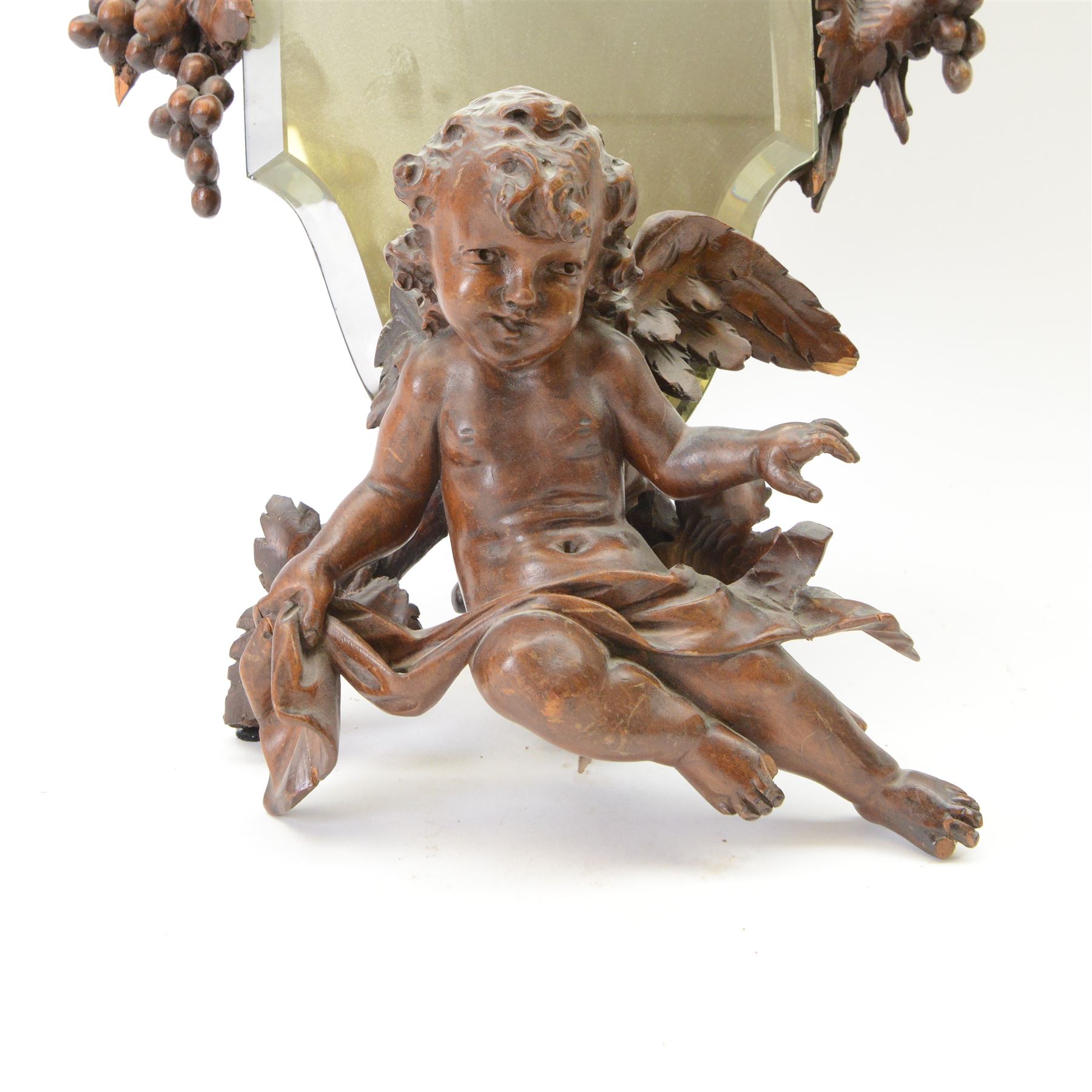 Late 19th century Continental carved wooden easel mirror, probably Black Forest, the shaped and bevelled mirror plate with surround carved with fruiting vines and surmounted with the figure of a cherub, with easel support verso, H72cm