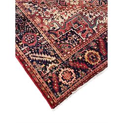 Persian Heriz crimson ground carpet, large central medallion comprising projecting palmettes with surrounding stylised plant motifs and trailing branches, the main border decorated with stylised leaf and flower head motifs within geometric pattern guard stripes